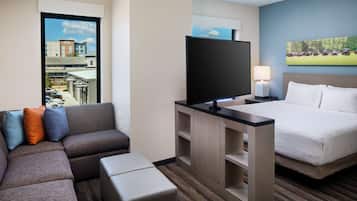 Ein Hotelzimmer mit einem großen Bett, einer Couch, einem Fernseher und einem Fenster mit Blick auf Gebäude.