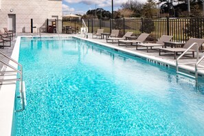 A rectangular pool with clear blue water, surrounded by a black fence and equipped with multiple lounge chairs.