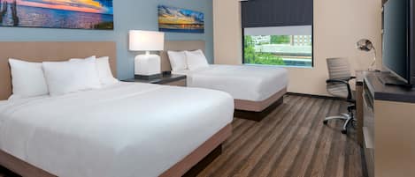 A hotel room with two beds, a desk with a computer, a TV, and two paintings on the wall.