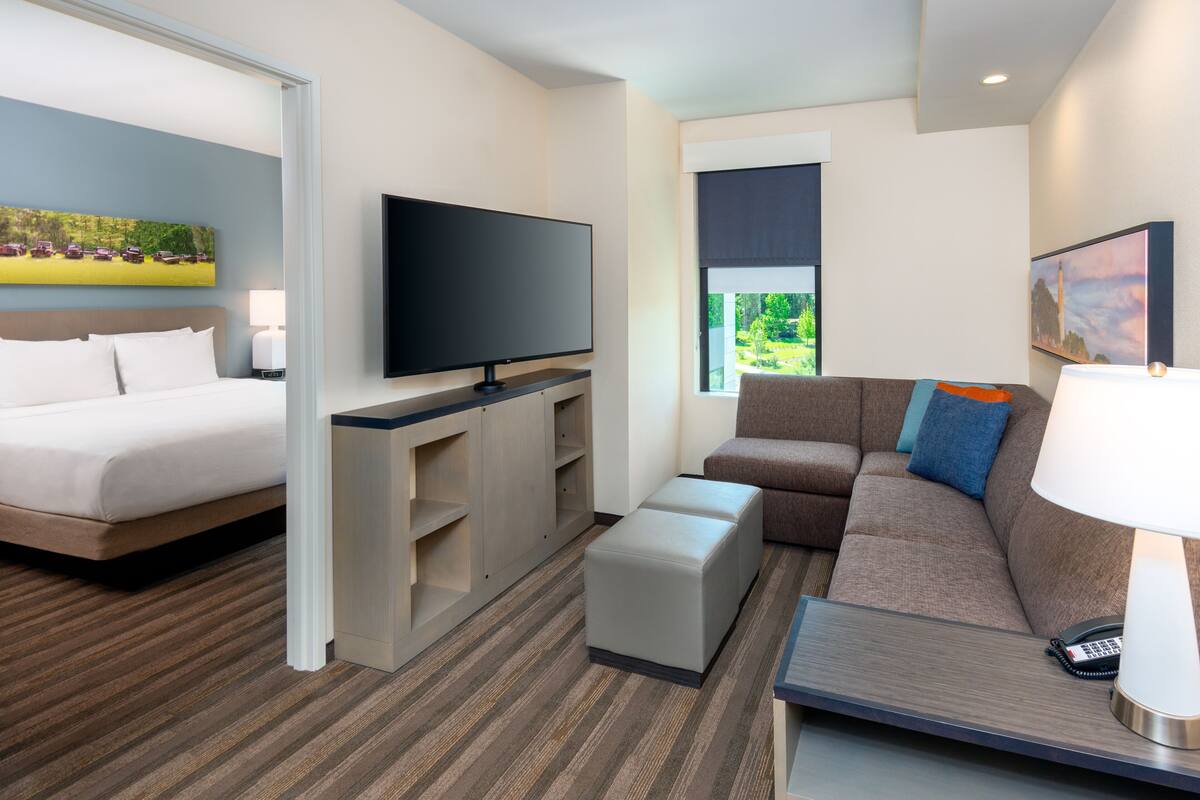 Habitación de hotel con cama, televisor, sofá y escritorio con lámpara.