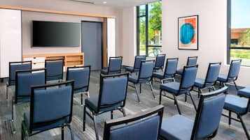 A conference room with rows of chairs, a large flat-screen TV, a wooden cabinet, and a large window with a view of greenery.