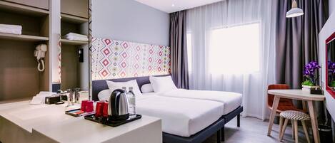 Una habitación de hotel con cama, mesita de noche, escritorio, silla y ventana con cortinas.