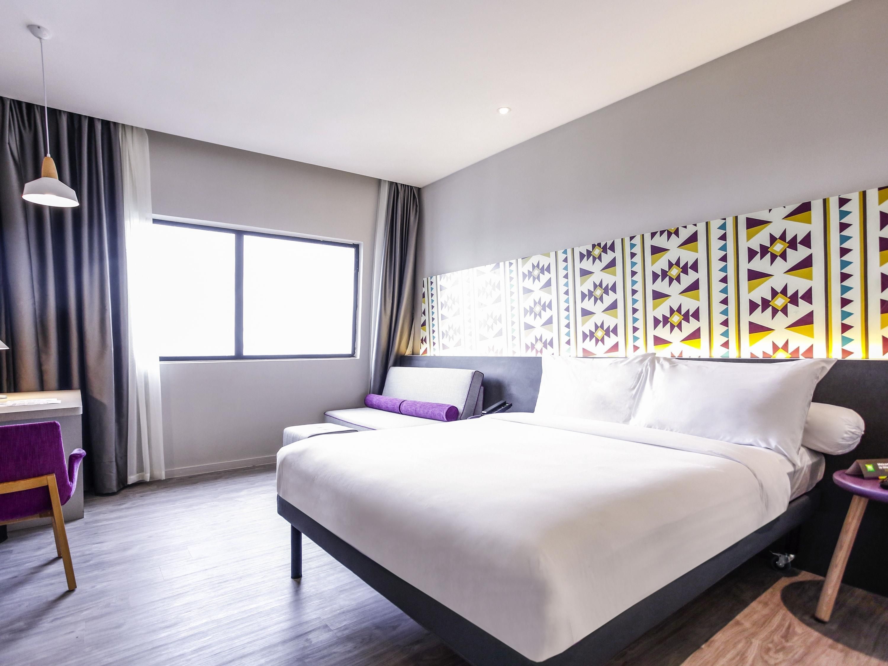 A modern hotel room with a large bed, a desk, and a window with curtains.