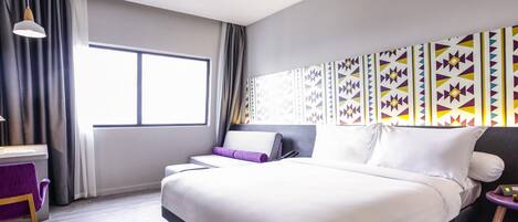 A modern hotel room with a large bed, a desk, and a window with curtains.
