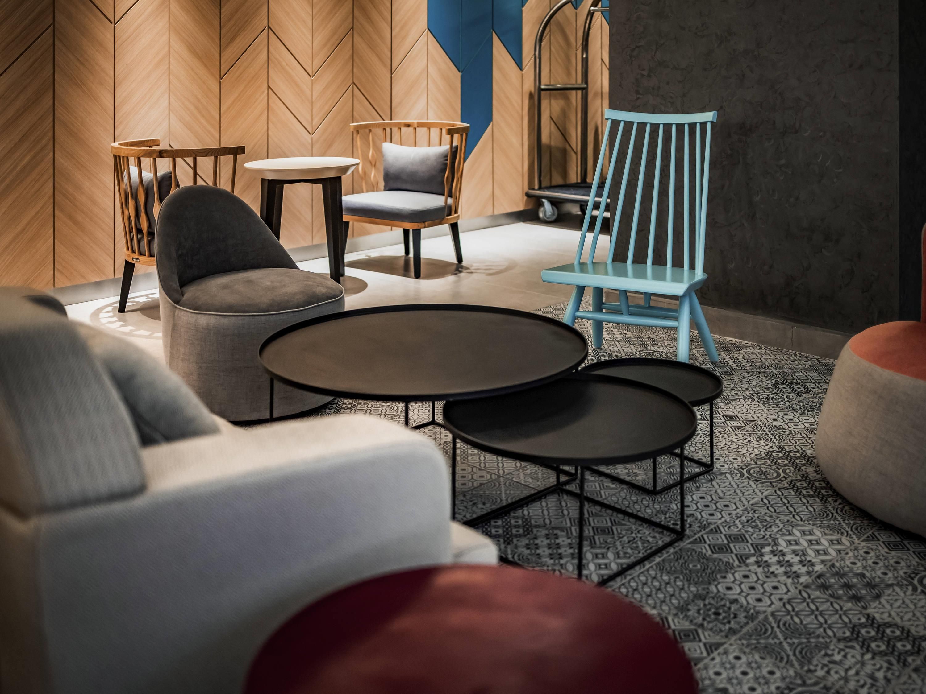 A modern lounge area with a herringbone wood wall, a blue chair, and a grey sofa.