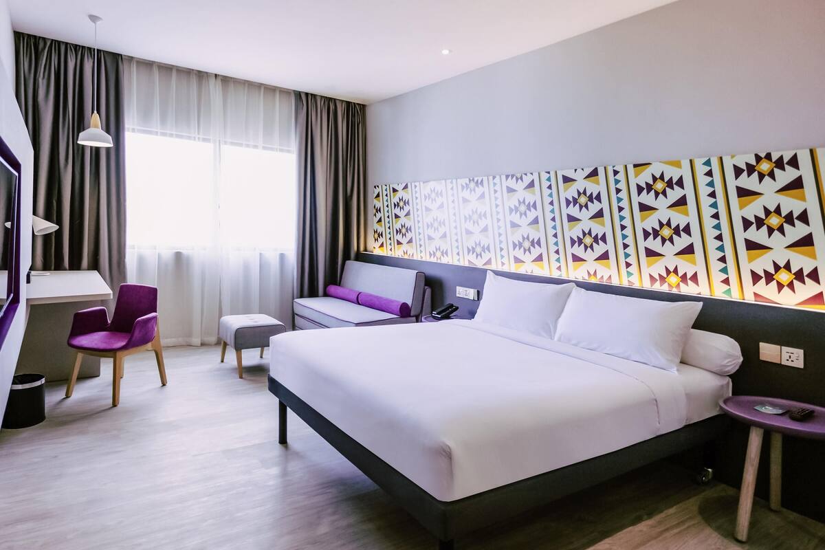 Una habitación de hotel moderna con una cama grande, un escritorio, una silla y una pared con detalles decorativos.