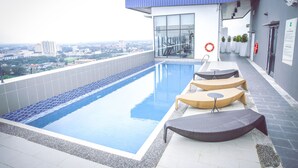 Una piscina en la azotea con sillones de descanso y vistas a la ciudad.