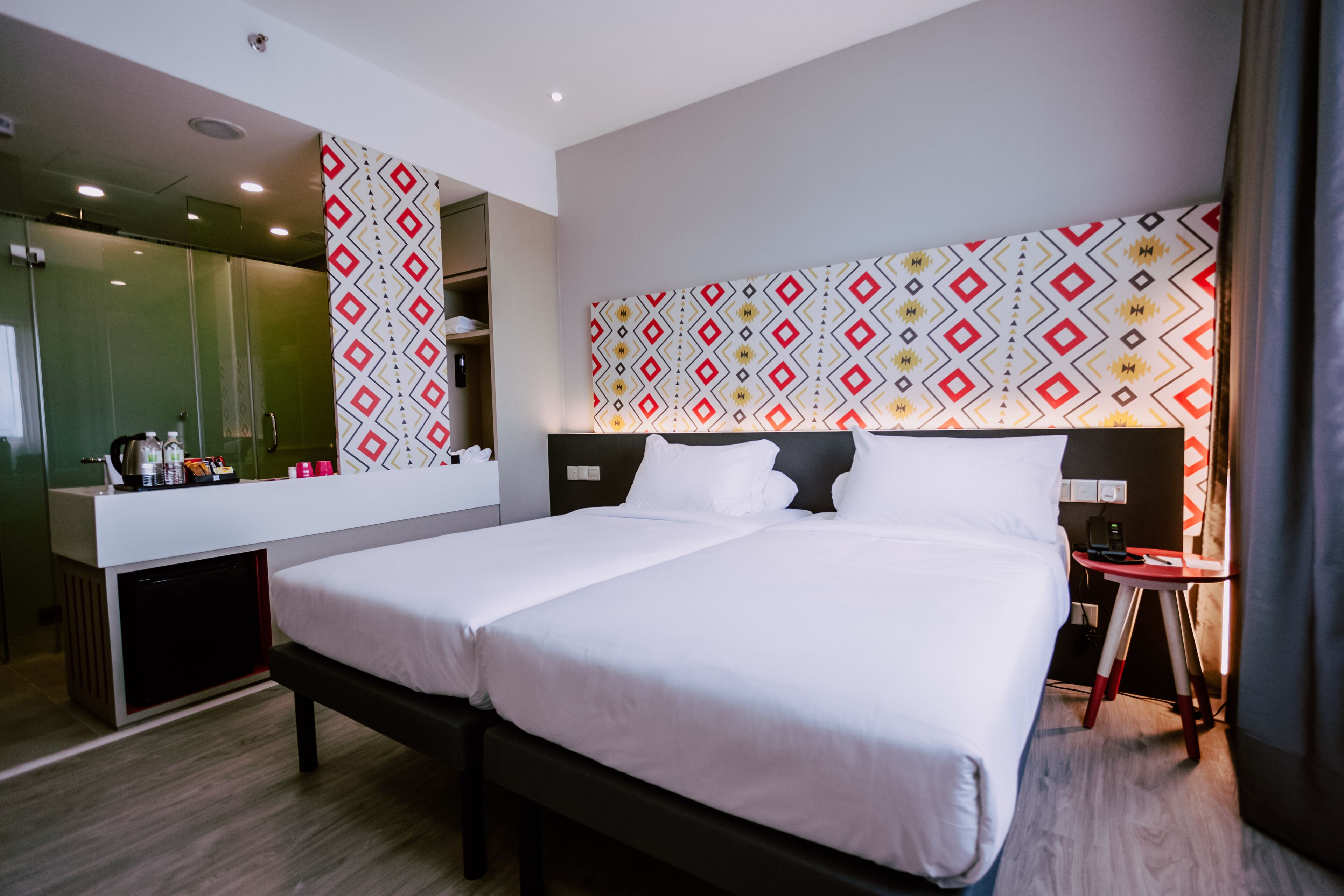 Ein modernes Hotelzimmer mit einem großen Bett, einem Nachttisch, einem Spiegel und einem gemusterten Kopfteil.