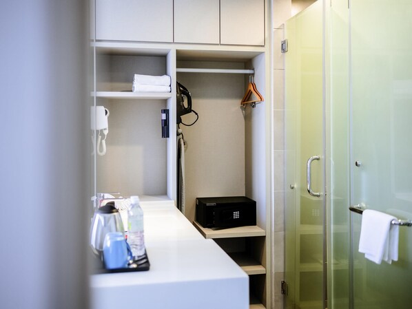 A hotel room with a white vanity, a black suitcase, a hairdryer, and a towel rack.