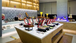 Un moderno vestíbulo de hotel con zona de buffet, mostrador de recepción y una pared decorativa con baldosas estampadas.