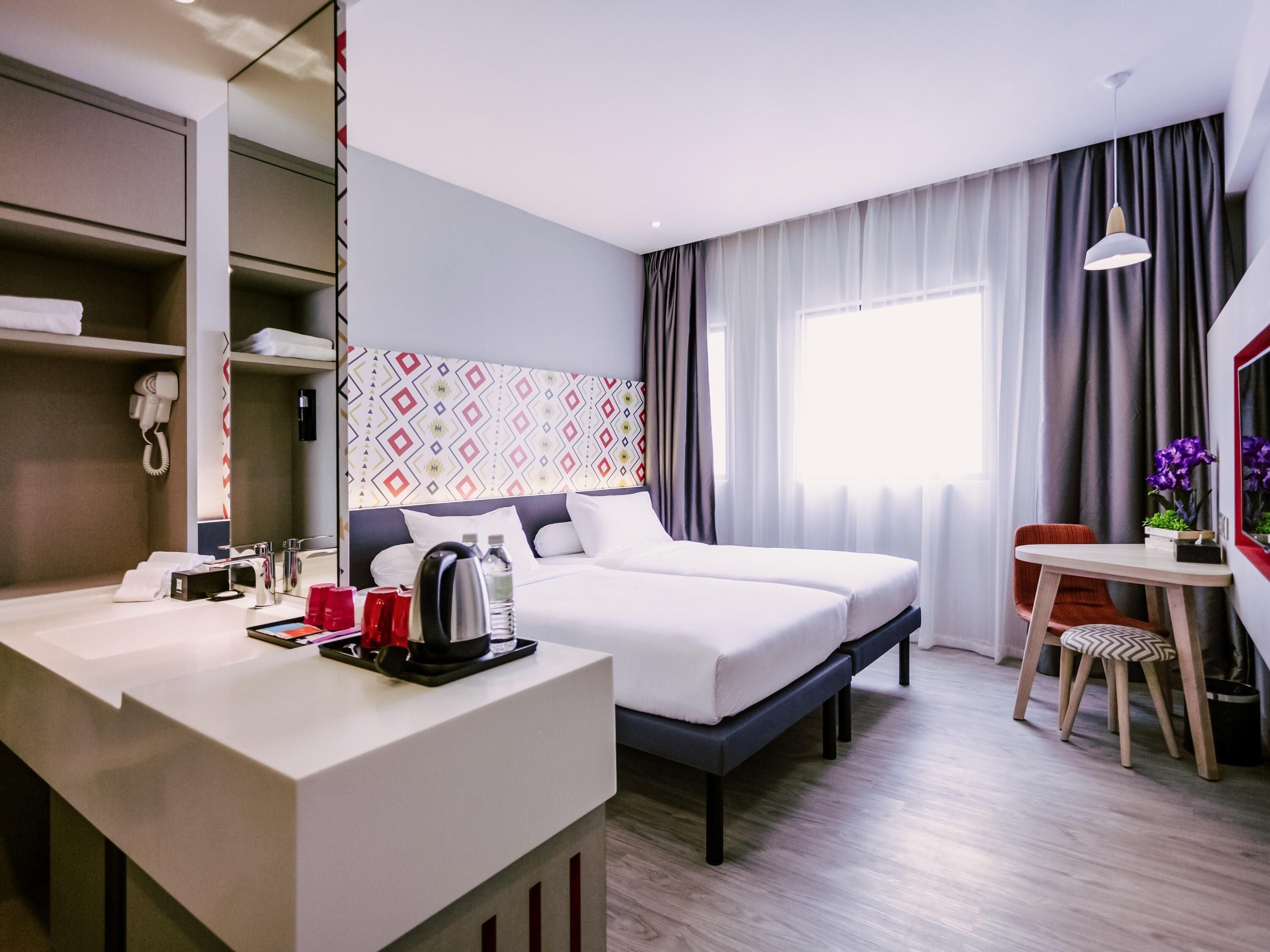 Una habitación de hotel con cama, mesita de noche, escritorio, silla y ventana con cortinas.