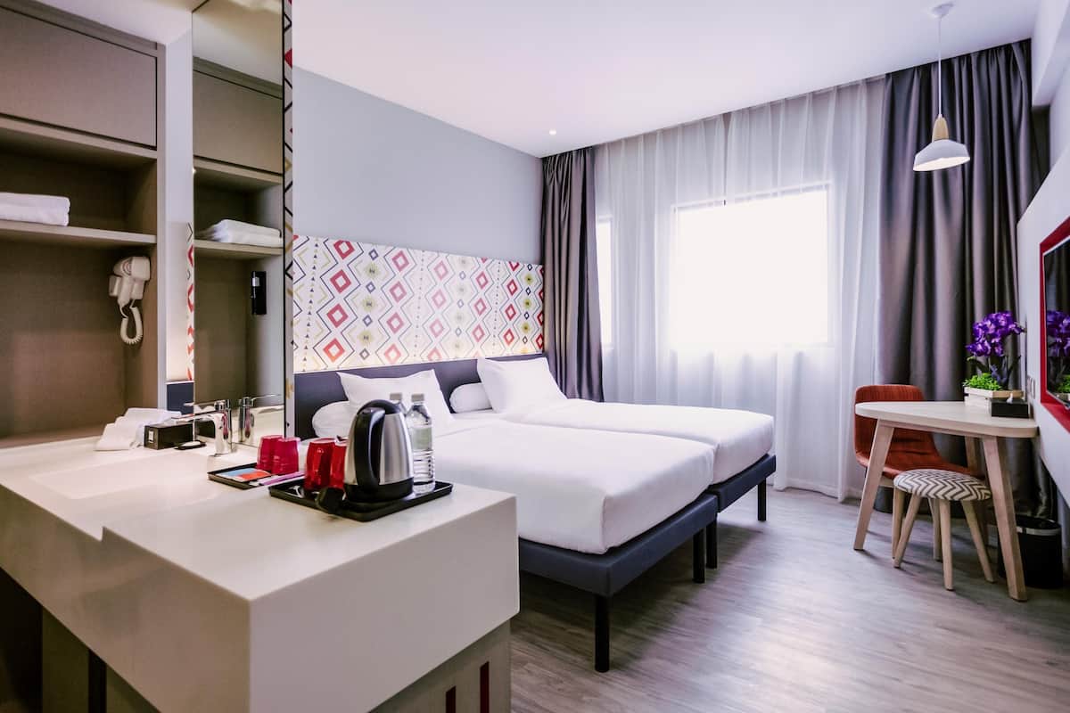 A hotel room with a bed, bedside table, desk, chair, and a window with curtains.
