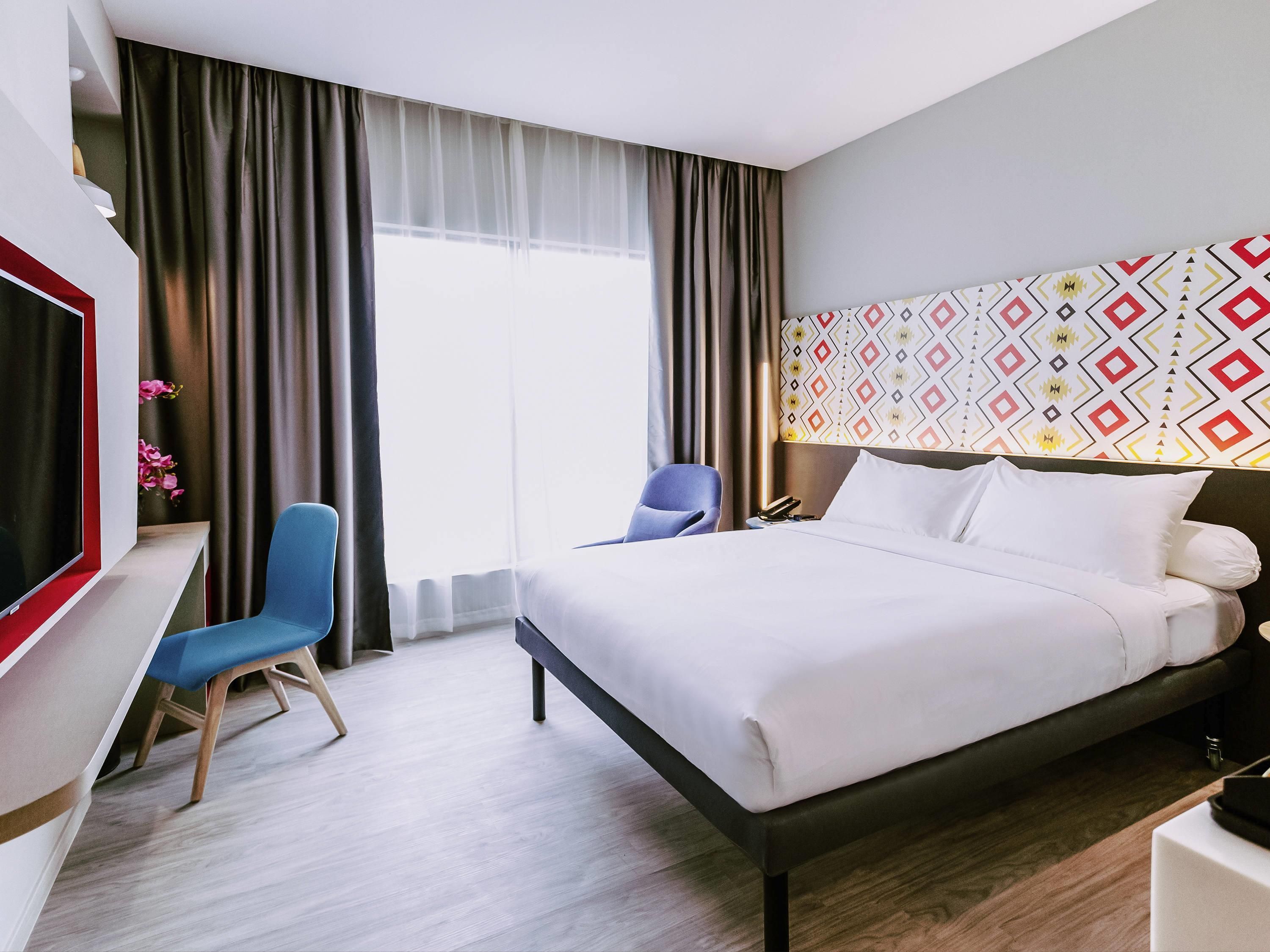 Ein Hotelzimmer mit Bett, Schreibtisch, Stuhl, Fernseher und einer Wand mit Muster.