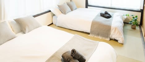 Two single beds with white bedding, a small potted plant, and a window with sheer curtains.