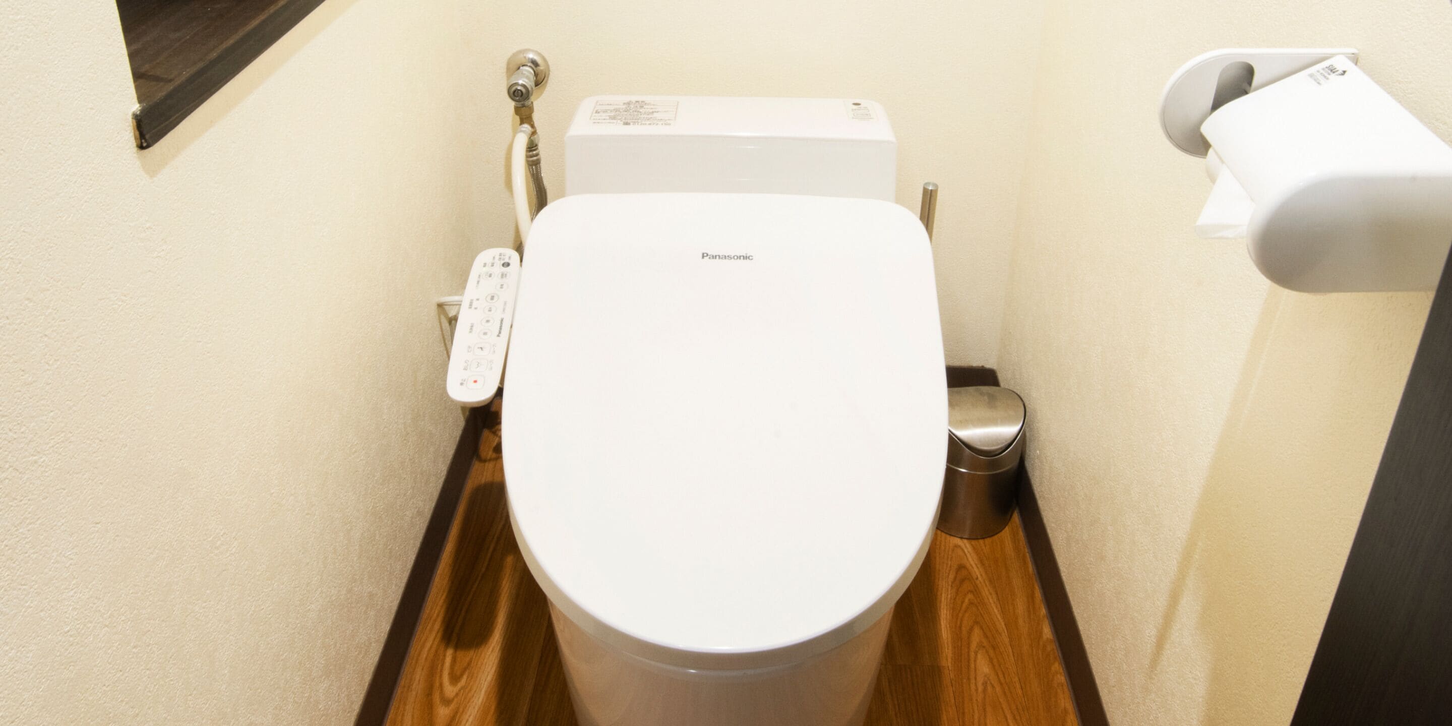 A compact bathroom with a white toilet, a control panel, and a bidet attachment.