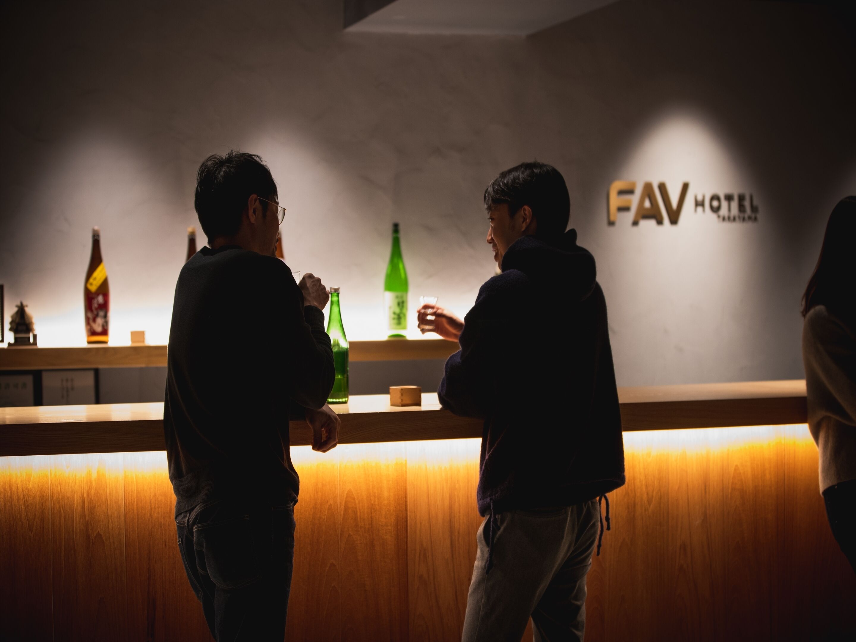 A bar area with wooden counter and shelves holding bottles.