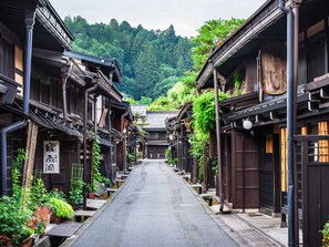 A traditional Japanese street with wooden buildings, a clear sky, and a mountain in the background. - fav HIDATAKAYAMA (Takayama)