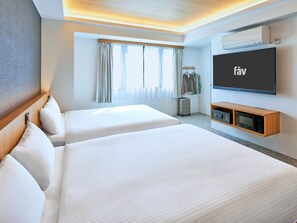 Hotellihuone, jossa on kaksi sänkyä, taulutelevisio, minibaari ja ikkuna, jossa on verhot.