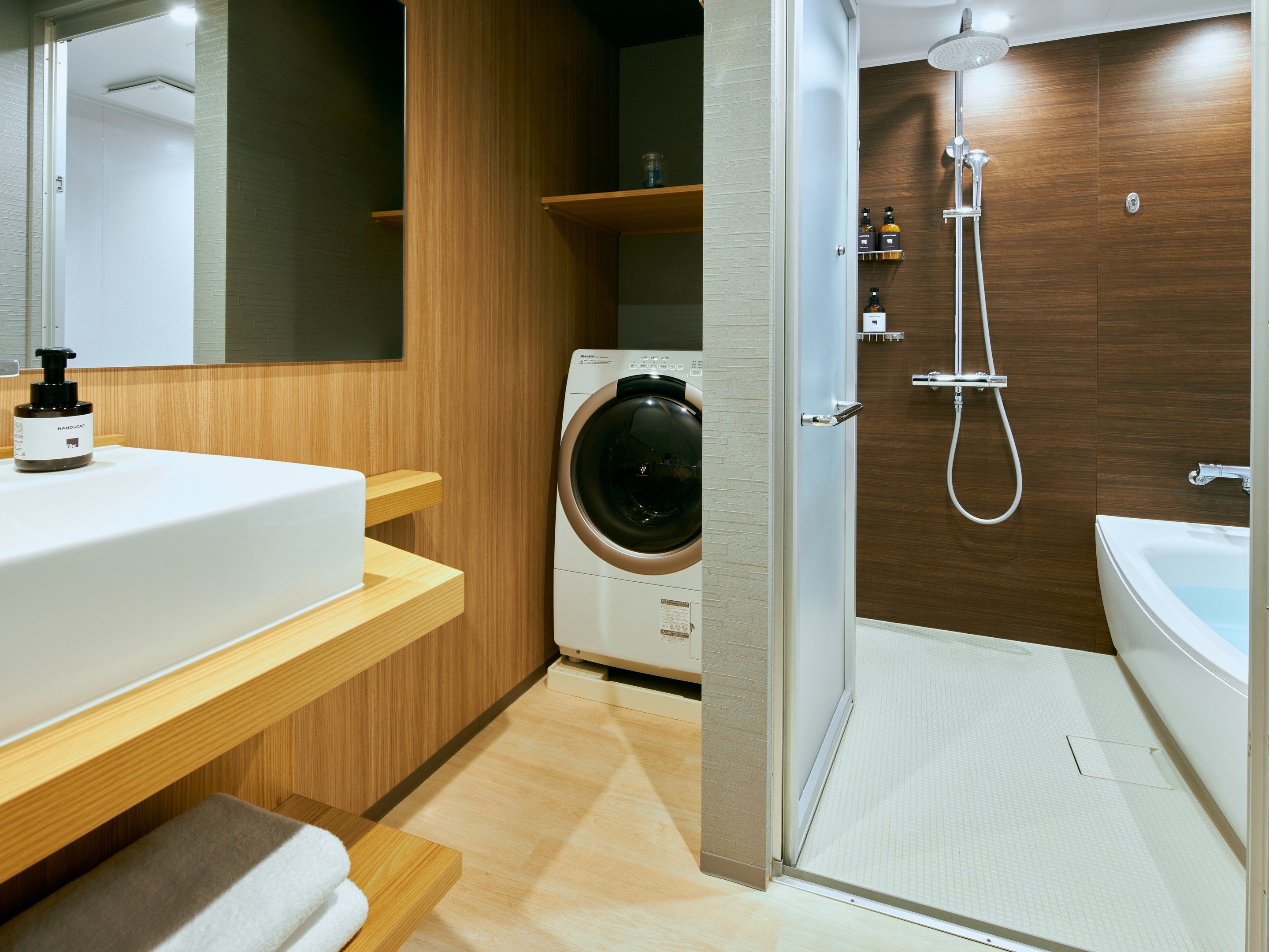 A modern bathroom with a built-in washing machine, a shower, and a sink with a soap dispenser.