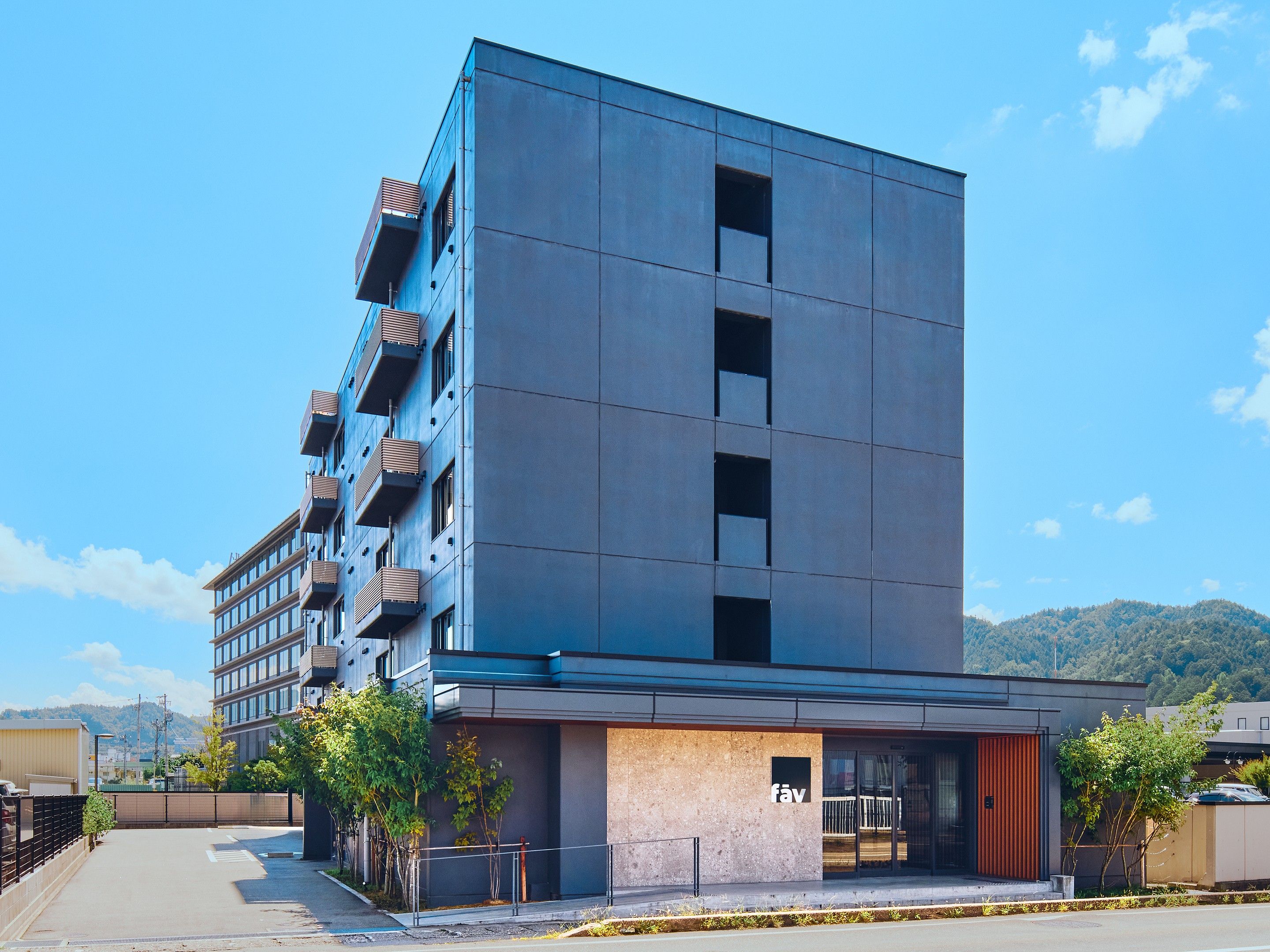 A modern building with a flat facade, multiple balconies, and a ground-level entrance with a visible sign.