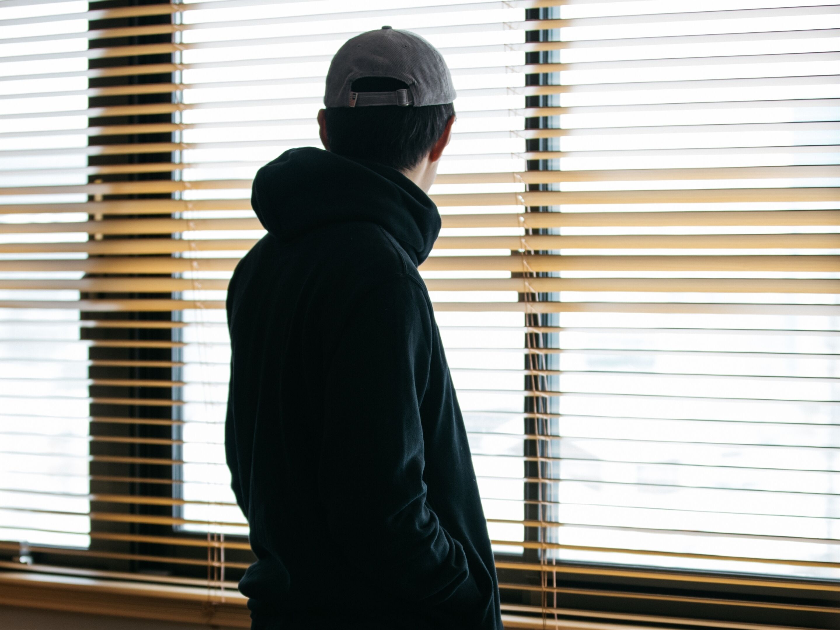 A person standing in front of a window with horizontal blinds.