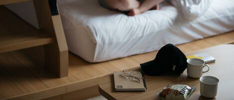 Una persona sentada en una cama con un cuaderno, gafas y una taza sobre una mesa de madera.