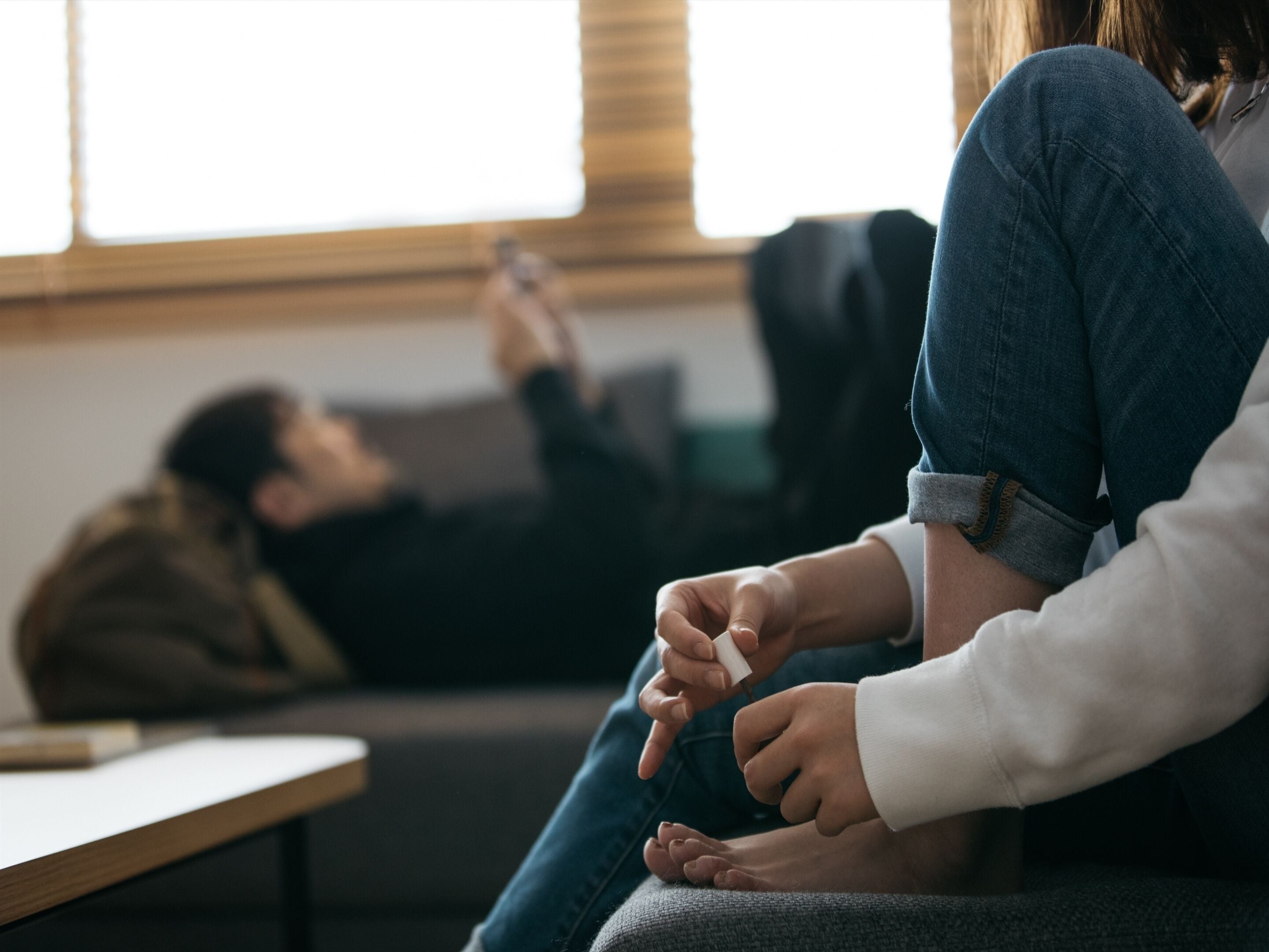 Eine Person sitzt auf einem Sofa, eine andere steht, und eine dritte Person liegt am Boden.