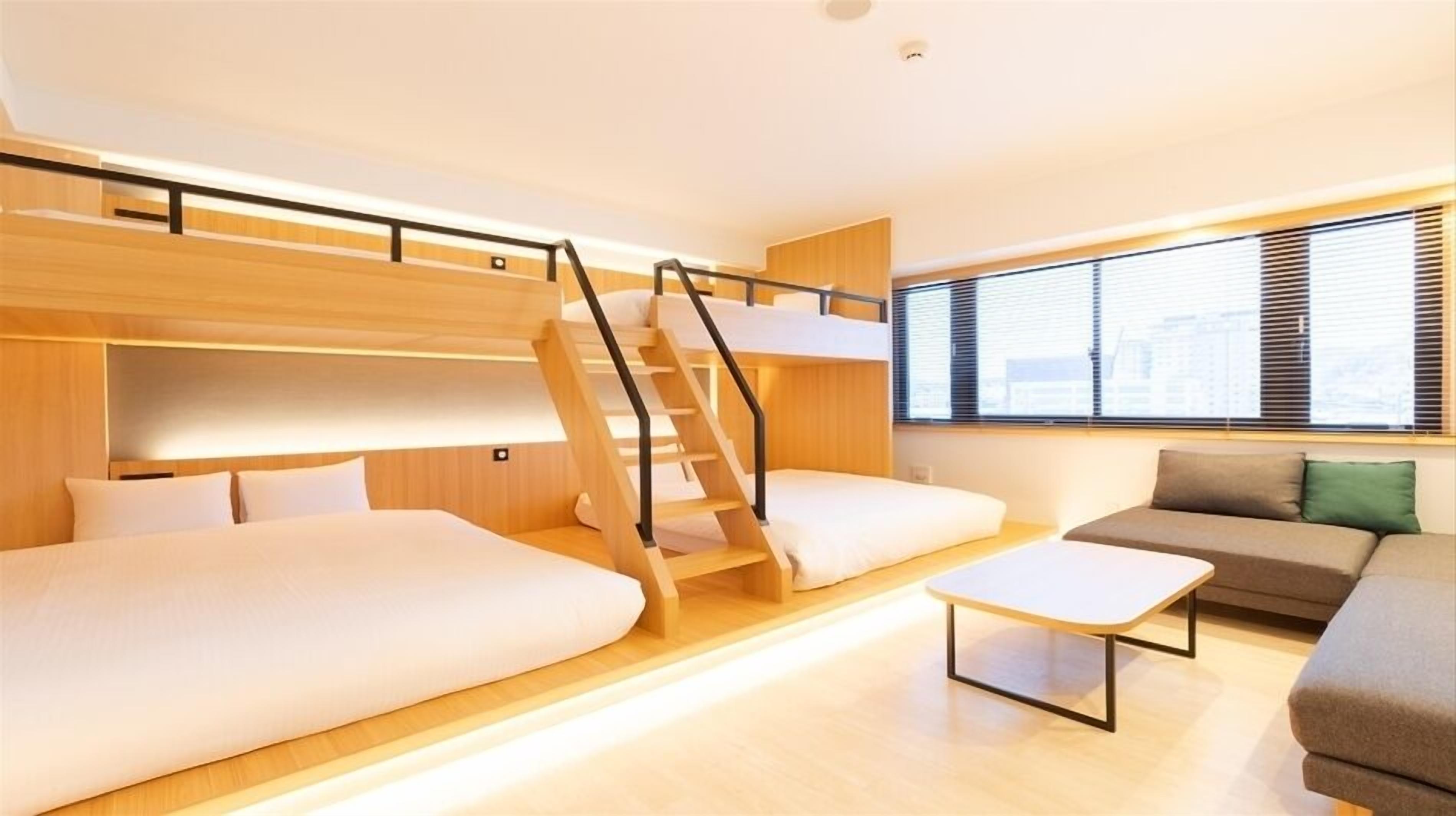Et moderne hotelværelse med køjeseng, sofa, sofabord og et vindue med rullegardiner.