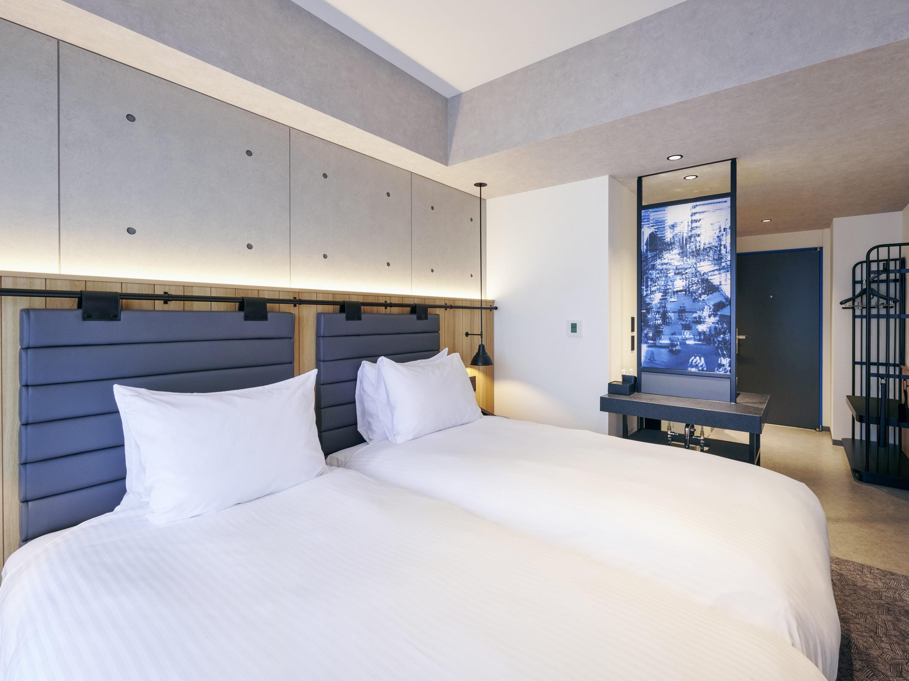 A modern hotel room with a large bed, a headboard with storage compartments, a bedside table, and a large mirror.