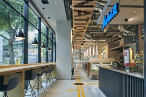 L’intérieur d’un café moderne, avec un long comptoir en bois, des tabourets de bar noirs et une vue dégagée grâce à de grandes fenêtres.