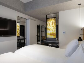 A modern hotel room with a large bed, a flat-screen TV, a desk with a chair, and a large mirror.