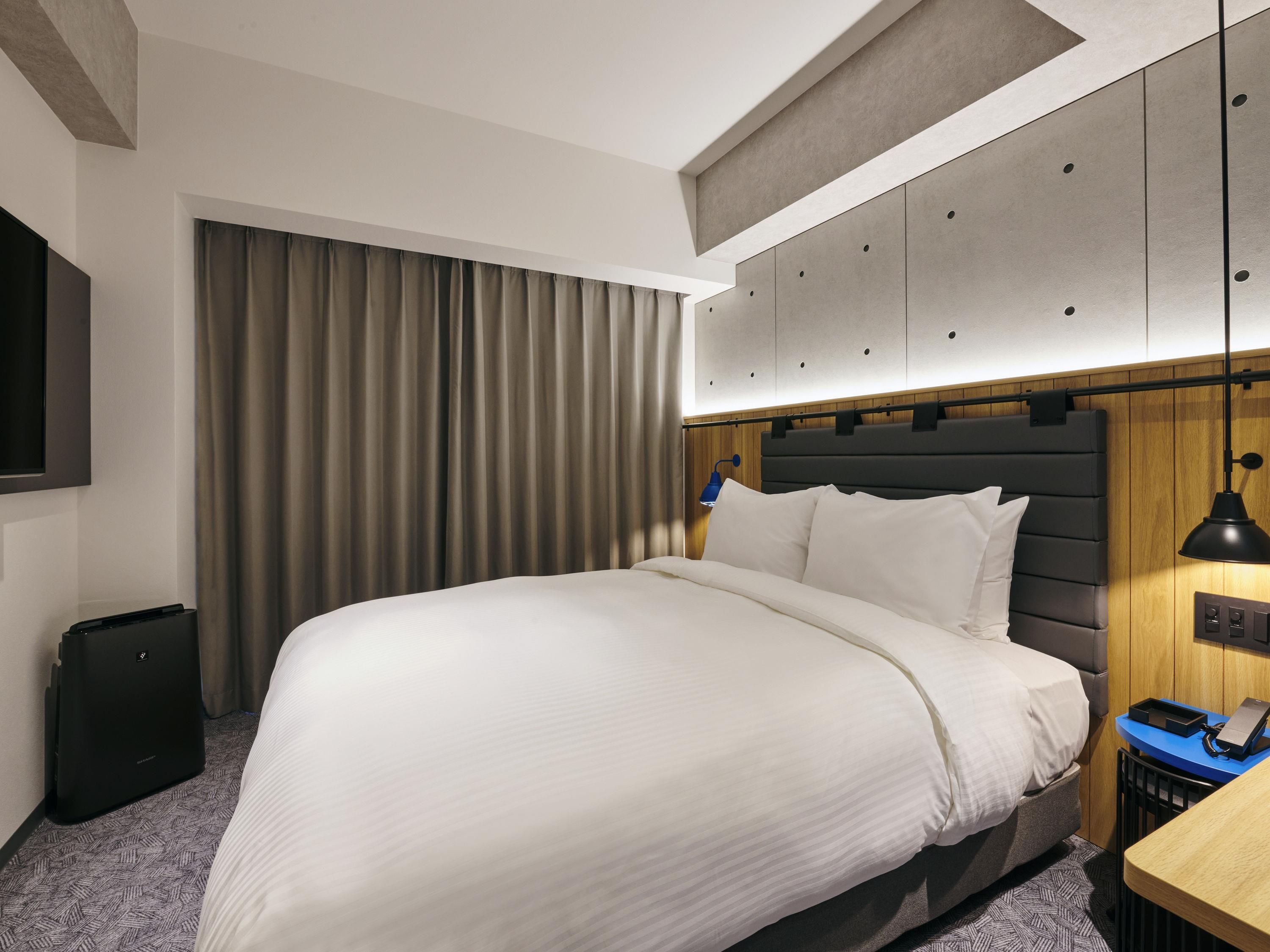 A hotel room with a large bed, a desk with a lamp, a wardrobe, and a television on the wall.