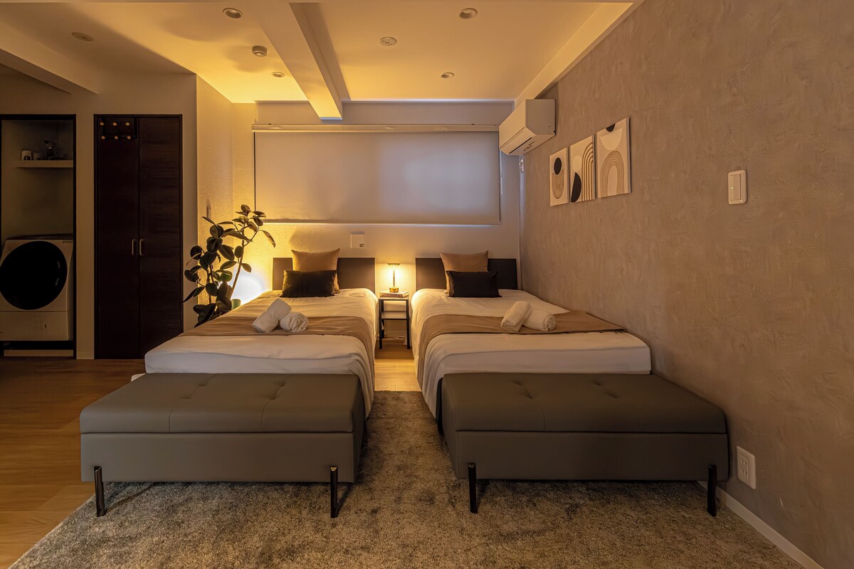 Una habitación de hotel moderna con dos camas, un ventanal grande, un ventilador de techo y una lavadora incorporada.