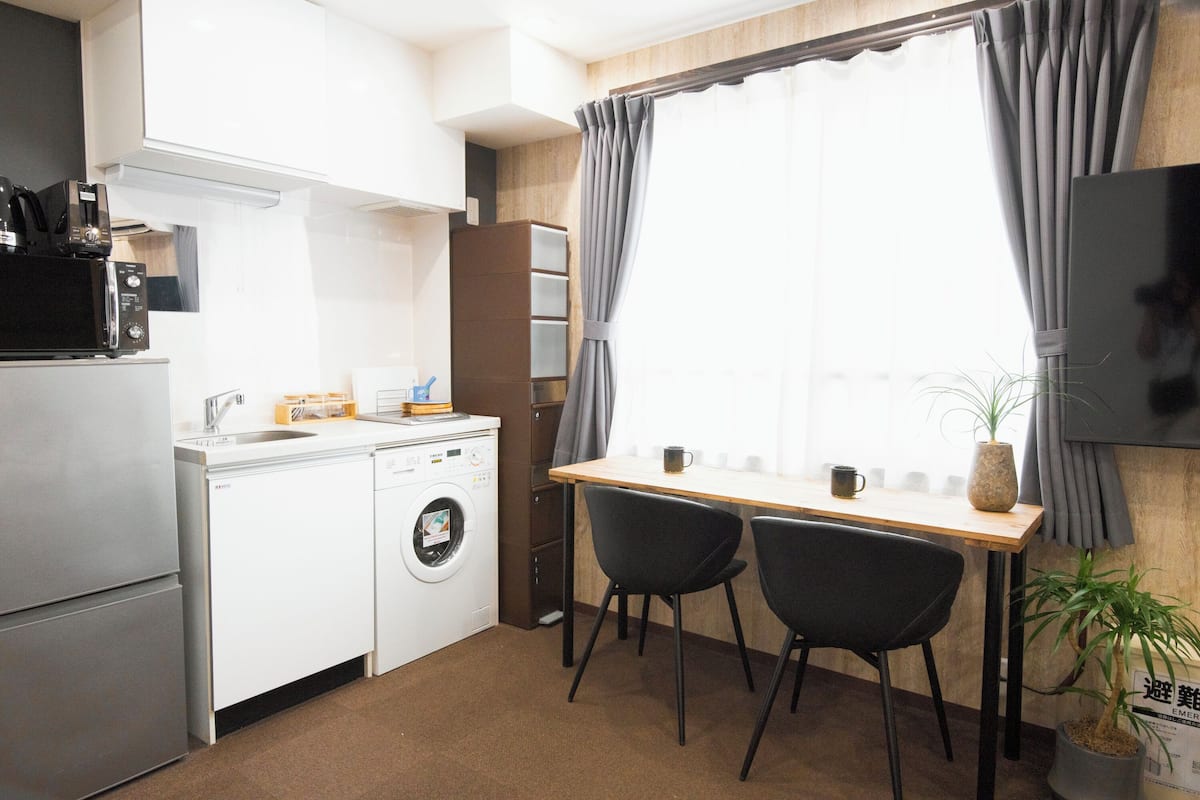 A compact kitchen with a washing machine, a microwave, and a small dining area with two chairs and a table.