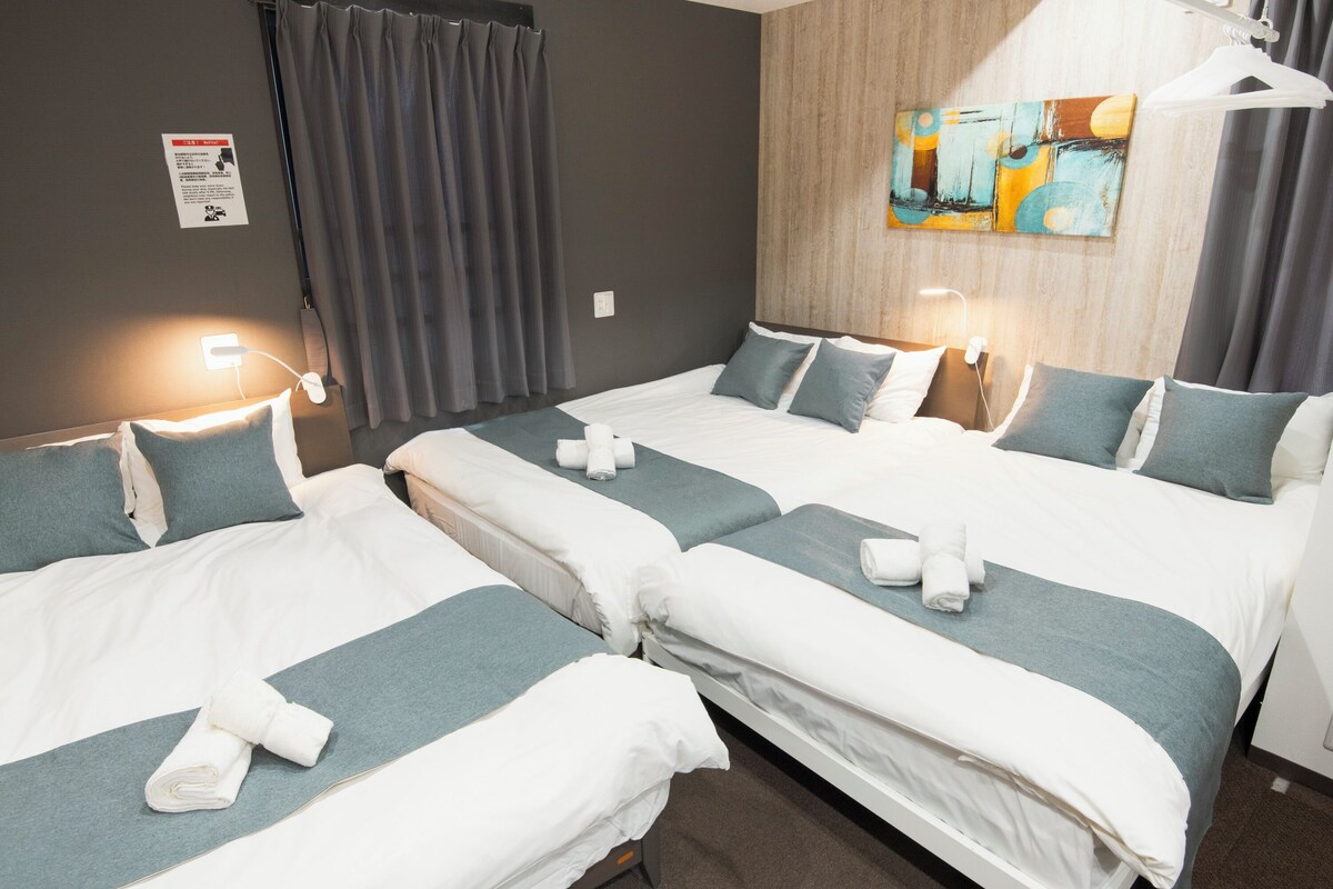 Habitación de hotel con dos camas, cortinas grises, una pared de acento de madera y un cuadro.
