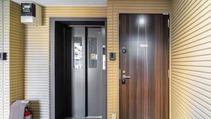 Een hotelentree met een houten deur, een brandblusser en een intercomsysteem voor beveiliging.