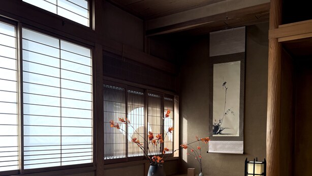 A traditional Japanese room with tatami flooring, a low wooden table, a vase with flowers, and a shoji screen with a view of the outside.