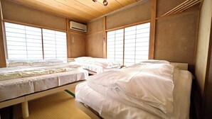 A traditional Japanese-style room with tatami flooring, three single beds, and sliding shoji doors.