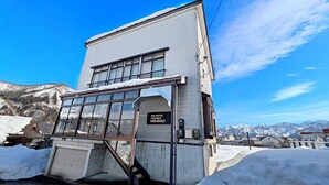 A hotel building with a sign reading "The Hotel Yuzawa Paradiso" and a view of snow-covered mountains in the background.