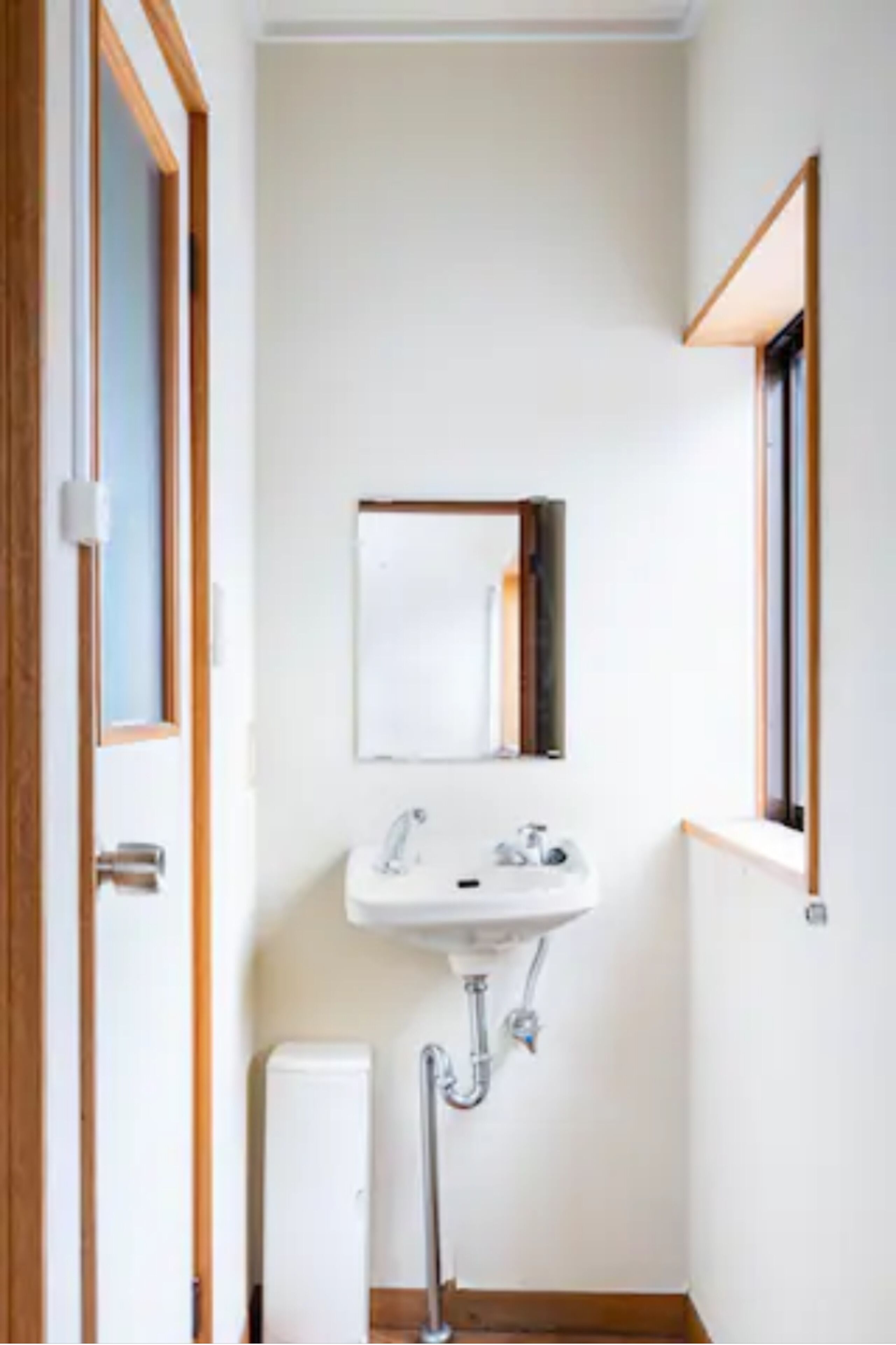 Une petite salle de bain propre, avec un lavabo blanc, un miroir et une fenêtre.