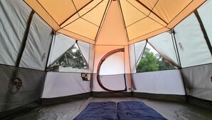 Tienda de campaña con entrada circular, una cama y vistas a árboles.