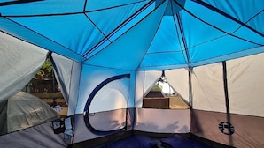 Una carpa con entrada circular, un área de descanso con cojines azules y vistas del entorno.
