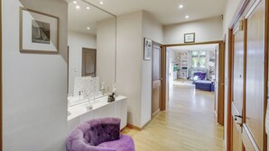 Un intérieur moderne avec une console blanche, un fauteuil violet et un couloir menant à un espace de vie comprenant un canapé et une table basse.