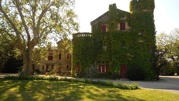 Un bâtiment historique aux murs couverts de lierre et surmonté d’une tourelle, entouré de pelouses et d’arbres bien entretenus.