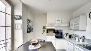 Une cuisine moderne avec des meubles blancs, un évier en acier inoxydable et un coin repas doté d’une table sombre.