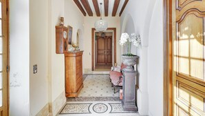 Un couloir avec une porte en bois, un lustre, un meuble en bois et un tapis à motifs.