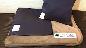 A bed with a dark blue pillow and a brown blanket with a tag. - Hotel Livemax Ikebukuroekimae (Tokyo)