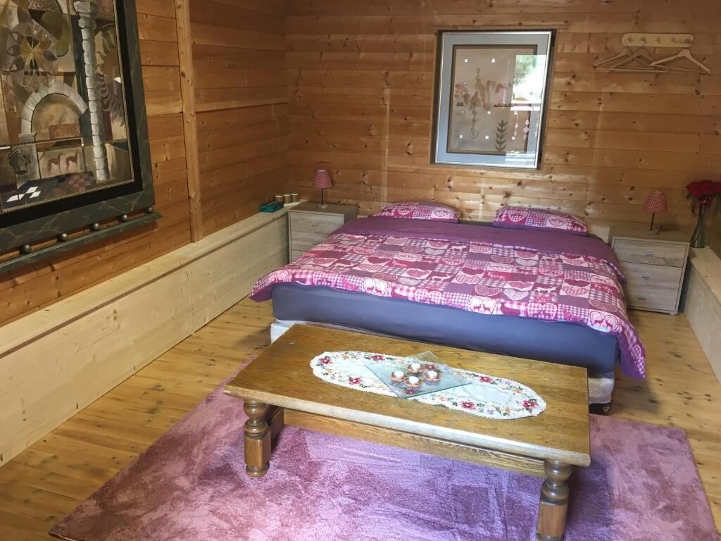 A wooden cabin bedroom with a bed, bedside tables, a framed picture, and a small table with a floral tablecloth.