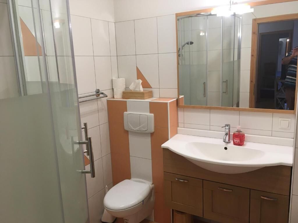 Un baño con cabina de ducha de vidrio, inodoro blanco, lavabo con espejo y mueble de madera debajo.