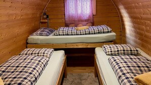 A cozy cabin room with two beds, a window with curtains, and a wooden ceiling. - Gasthof Rafting Alm (Haiming)